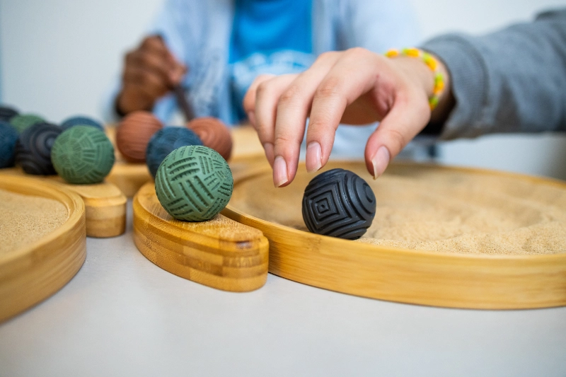 Closeup of a student's hands using Cobozen spheres in a sand Zen garden.